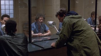Movie still from “The Fugitive” (1993), directed by Andrew Davis – A man sitting in front of a mirror talking to another man in front of a window; Medium shot, Over the shoulder angle