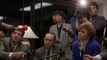 Movie still from “The Fugitive” (1993), directed by Andrew Davis – A woman in a hat is holding a microphone; Medium shot, Over the shoulder angle