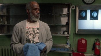 Movie still from “The Fugitive” (1993), directed by Andrew Davis – An older man holding a pair of blue towels in a room; Medium shot, Low angle
