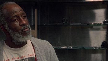 Movie still from “The Fugitive” (1993), directed by Andrew Davis – An older man with a gray beard is standing in front of a shelf; Close Up shot, Over the shoulder angle