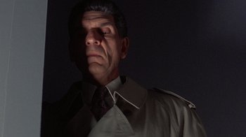 Movie still from “The Fugitive” (1993), directed by Andrew Davis – A man wearing a trench coat and a neck tie; Close Up shot, Low angle