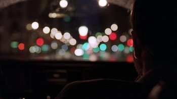 Movie still from “The Fugitive” (1993), directed by Andrew Davis – A person sitting in a car at night with lights in the background; Close Up shot, Over the shoulder angle