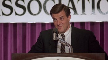 Movie still from “The Fugitive” (1993), directed by Andrew Davis – A man wearing a suit and tie talking into a microphone; Close Up shot, High angle