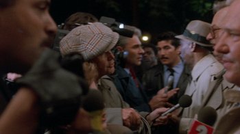 Movie still from “The Fugitive” (1993), directed by Andrew Davis – A group of people standing around each other holding microphones; Close Up shot, Over the shoulder angle