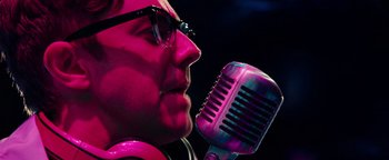 Movie still from “Popstar: Never Stop Never Stopping” (2016), directed by Akiva Schaffer – A man with glasses and a microphone in front of his face; Close Up shot, Low angle