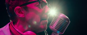 Movie still from “Popstar: Never Stop Never Stopping” (2016), directed by Akiva Schaffer – A man with glasses is singing into a microphone; Extreme Close Up shot, Low angle