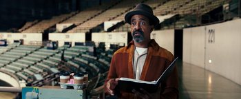Movie still from “Popstar: Never Stop Never Stopping” (2016), directed by Akiva Schaffer – A man holding a book while standing in an arena; Medium shot, High angle