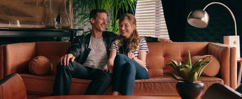 Movie still from “Popstar: Never Stop Never Stopping” (2016), directed by Akiva Schaffer – A man and a woman sitting on top of a brown couch; Medium shot, High angle