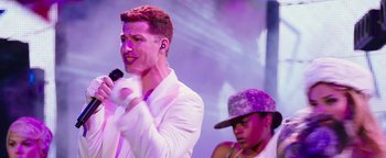 Movie still from “Popstar: Never Stop Never Stopping” (2016), directed by Akiva Schaffer – A man in white jacket holding a microphone and another man in purple hat; Medium shot, Over the shoulder angle