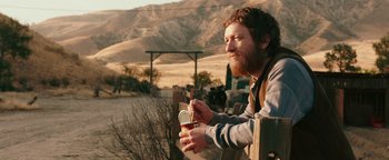 Movie still from “Popstar: Never Stop Never Stopping” (2016), directed by Akiva Schaffer – A man holding a can of soda while sitting on a fence; Medium shot, Over the shoulder angle