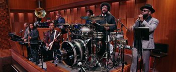 Movie still from “Popstar: Never Stop Never Stopping” (2016), directed by Akiva Schaffer – A group of people playing drums in a room; Wide shot, Low angle