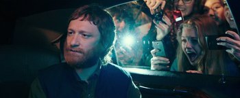 Movie still from “Popstar: Never Stop Never Stopping” (2016), directed by Akiva Schaffer – A man sitting in front of a mirror holding a cell phone; Close Up shot, Over the shoulder angle