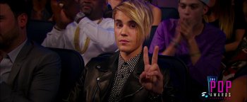 Movie still from “Popstar: Never Stop Never Stopping” (2016), directed by Akiva Schaffer – A man in a leather jacket holding up a peace sign; Close Up shot, Over the shoulder angle