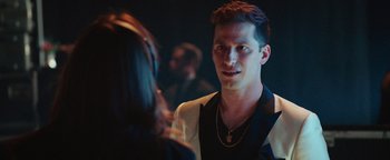 Movie still from “Popstar: Never Stop Never Stopping” (2016), directed by Akiva Schaffer – A man in a black and white shirt is talking to a woman in a black dress; Close Up shot, Over the shoulder angle