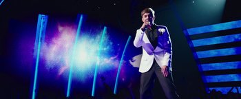 Movie still from “Popstar: Never Stop Never Stopping” (2016), directed by Akiva Schaffer – A man in a white jacket is on stage singing; Medium shot, Low angle