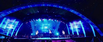 Movie still from “Popstar: Never Stop Never Stopping” (2016), directed by Akiva Schaffer – A group of men standing on a stage in front of a crowd; Extreme Wide shot, Low angle