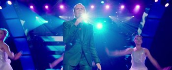 Movie still from “Popstar: Never Stop Never Stopping” (2016), directed by Akiva Schaffer – A man in a black suit is holding a microphone; Medium shot, Low angle