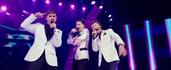 Movie still from “Popstar: Never Stop Never Stopping” (2016), directed by Akiva Schaffer – A group of men singing on a stage with purple lighting; Medium shot, Low angle