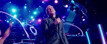 Movie still from “Popstar: Never Stop Never Stopping” (2016), directed by Akiva Schaffer – A man in a gray suit is singing into a microphone; Medium shot, Low angle