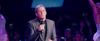 Movie still from “Popstar: Never Stop Never Stopping” (2016), directed by Akiva Schaffer – A man holding a microphone while wearing a suit and tie; Close Up shot, Over the shoulder angle