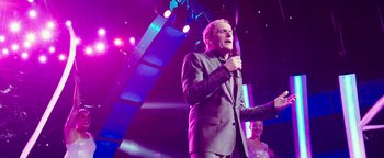 Movie still from “Popstar: Never Stop Never Stopping” (2016), directed by Akiva Schaffer – A man holding a microphone while standing next to a woman; Medium shot, Low angle