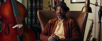 Movie still from “Popstar: Never Stop Never Stopping” (2016), directed by Akiva Schaffer – An older man sitting in a chair wearing a hat; Medium shot, Over the shoulder angle