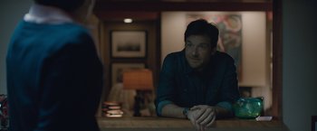 Movie still from “The Gift” (2015), directed by Joel Edgerton – A man sitting at a counter in front of a lamp; Medium shot, Over the shoulder angle