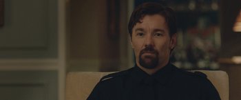 Movie still from “The Gift” (2015), directed by Joel Edgerton – A person sitting on a couch wearing a uniform; Close Up shot, Over the shoulder angle