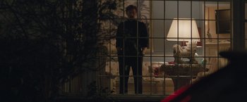 Movie still from “The Gift” (2015), directed by Joel Edgerton – A man standing behind bars in front of a living room; Wide shot, Over the shoulder angle