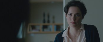 Movie still from “The Gift” (2015), directed by Joel Edgerton – A woman is looking at the camera while standing in front of a bookshelf; Close Up shot, Over the shoulder angle