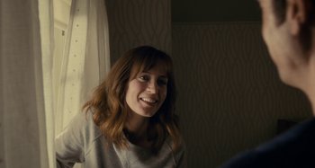 Movie still from “The Girl on the Train” (2016), directed by Tate Taylor – A woman with long red hair smiles at the camera; Medium shot, Over the shoulder angle