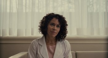 Movie still from “The Girl on the Train” (2016), directed by Tate Taylor – A woman in a white lab coat sitting on a couch; Close Up shot, Over the shoulder angle