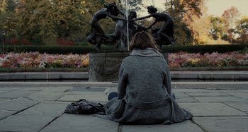 Movie still from “The Girl on the Train” (2016), directed by Tate Taylor – A woman sitting on the ground in front of a fountain; Wide shot, High angle