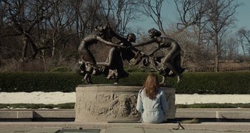 Movie still from “The Girl on the Train” (2016), directed by Tate Taylor – A woman sitting in front of a statue; Wide shot, High angle