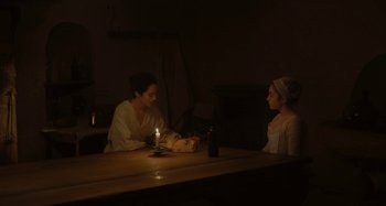 Movie still from “Portrait of a Lady on Fire” (2019), directed by Céline Sciamma – Two women sitting at a table with a lit candle; Medium shot, High angle