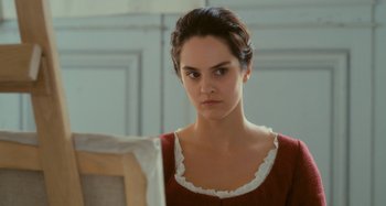 Movie still from “Portrait of a Lady on Fire” (2019), directed by Céline Sciamma – A woman in a red and white dress looking at the camera; Close Up shot, Over the shoulder angle