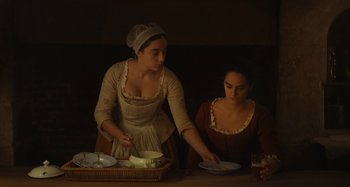 Movie still from “Portrait of a Lady on Fire” (2019), directed by Céline Sciamma – Two women are preparing food in a dimly - lit room; Medium shot, Low angle