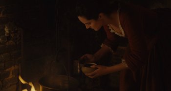 Movie still from “Portrait of a Lady on Fire” (2019), directed by Céline Sciamma – A woman in a red dress stirring something in a pot; Medium shot, High angle