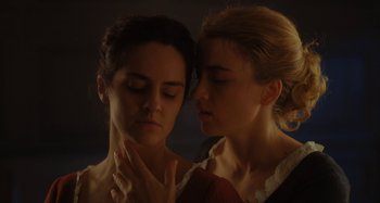 Movie still from “Portrait of a Lady on Fire” (2019), directed by Céline Sciamma – Two young women standing next to each other in a dark room; Close Up shot, High angle