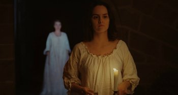Movie still from “Portrait of a Lady on Fire” (2019), directed by Céline Sciamma – A woman holding a lit candle in front of a woman in a white dress; Medium shot, Over the shoulder angle