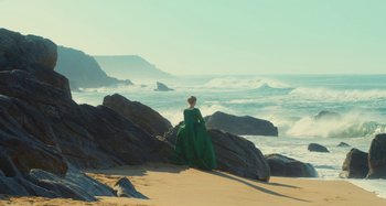 Movie still from “Portrait of a Lady on Fire” (2019), directed by Céline Sciamma – A woman in a green dress sitting on a rock on the beach; Extreme Wide shot, High angle