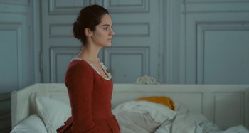 Movie still from “Portrait of a Lady on Fire” (2019), directed by Céline Sciamma – A woman in a red dress standing on a bed; Medium shot, Over the shoulder angle