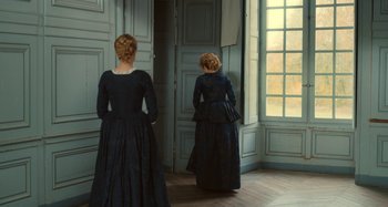 Movie still from “Portrait of a Lady on Fire” (2019), directed by Céline Sciamma – Two women dressed in period clothing standing in front of a window; Wide shot, Over the shoulder angle