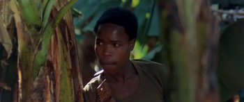 Movie still from “The Gods Must Be Crazy” (1980), directed by Jamie Uys – A young man holding a stick in the woods; Close Up shot, Over the shoulder angle