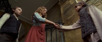 Movie still from “The Golden Compass” (2007), directed by Chris Weitz – A woman in a red dress is holding the hand of another woman; Medium shot, Low angle