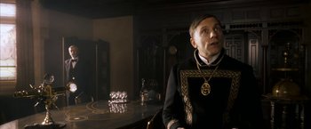 Movie still from “The Golden Compass” (2007), directed by Chris Weitz – A man sitting at a table in a dark room; Close Up shot, Low angle