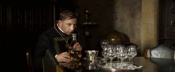 Movie still from “The Golden Compass” (2007), directed by Chris Weitz – A man sitting at a table with a wine glass; Medium shot, Low angle