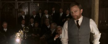 Movie still from “The Golden Compass” (2007), directed by Chris Weitz – A group of men in suits and ties in front of a crowd; Medium shot, Over the shoulder angle