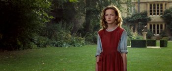 Movie still from “The Golden Compass” (2007), directed by Chris Weitz – A girl in a red dress stands in the grass; Medium shot, Over the shoulder angle