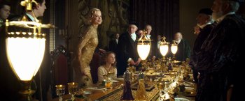 Movie still from “The Golden Compass” (2007), directed by Chris Weitz – A group of people standing around a table with food on it; Medium shot, Over the shoulder angle